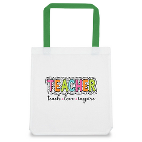 A white tote bag with green handles featuring a colorful text design that reads 'TEACHER' with a decorative pattern and the words 'teach', 'love', 'inspire' in a smaller font.