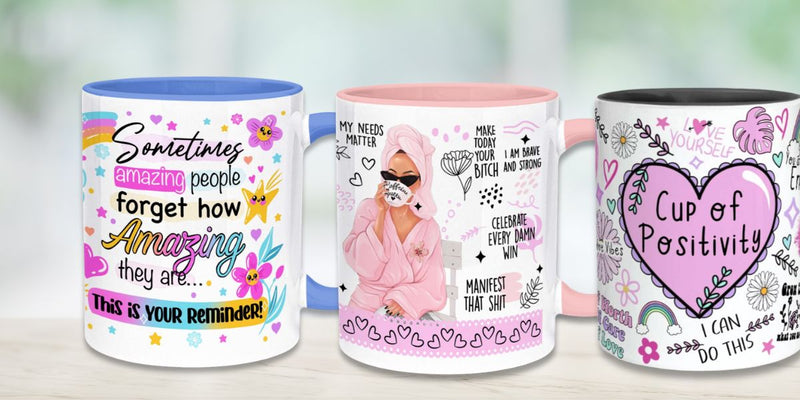 Colourful motivational coffee mugs set on a light table—left mug with blue rim reads ‘Sometimes amazing people forget how amazing they are,’ centre pink-rim mug shows a woman in a robe with self-care and empowerment quotes, right black-rim mug features a heart labeled ‘Cup of Positivity’; inspirational affirmation gift cups for women, teens, self-love and positivity.