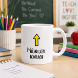 White mug with a yellow arrow and text on a desk with educational items in the background